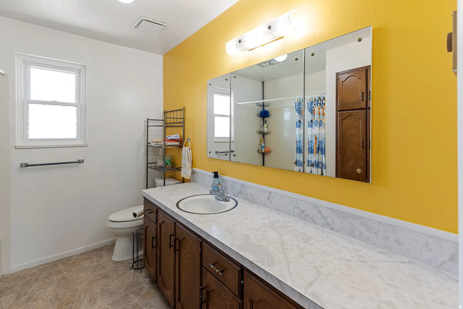 Vanity with wood-finish cabinetry and a white countertop, featuring an integrated sink, illuminated by an overhead light fixture