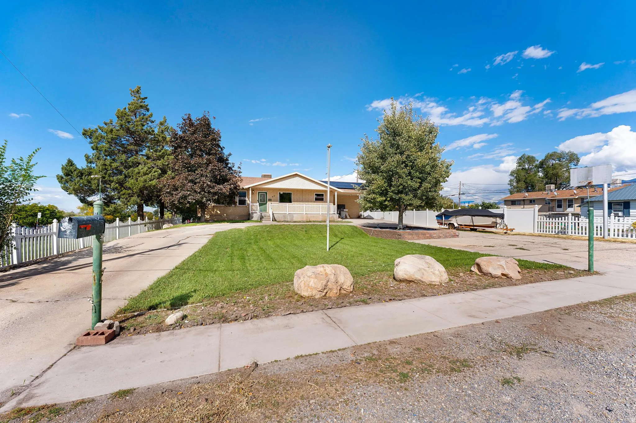 Expansive concrete driveway, mature landscaping, white picket fencing, and a front porch
