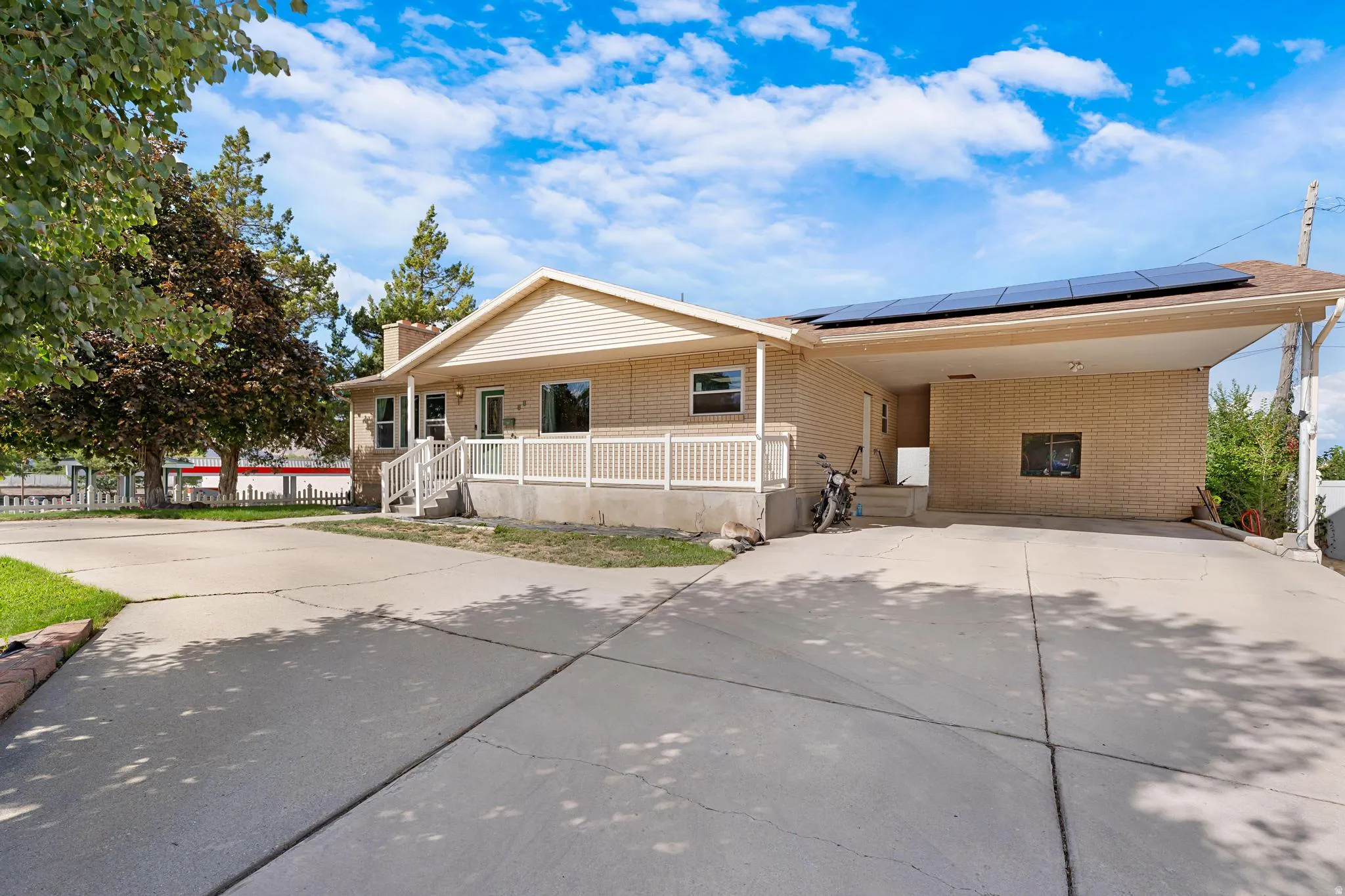 Brick exterior with a covered carport, covered porch, solar panels, and concrete driveway