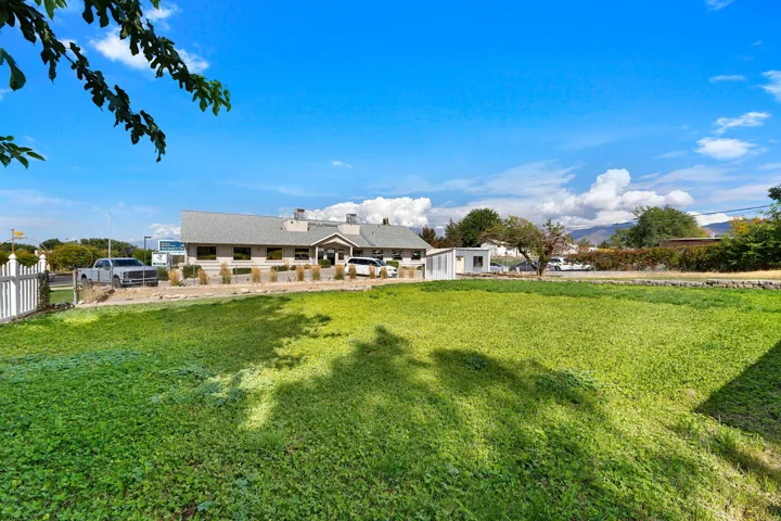Expansive green space with distant mountain backdrop, a white picket fence, and a neutral-toned building with a grey shingle roof
