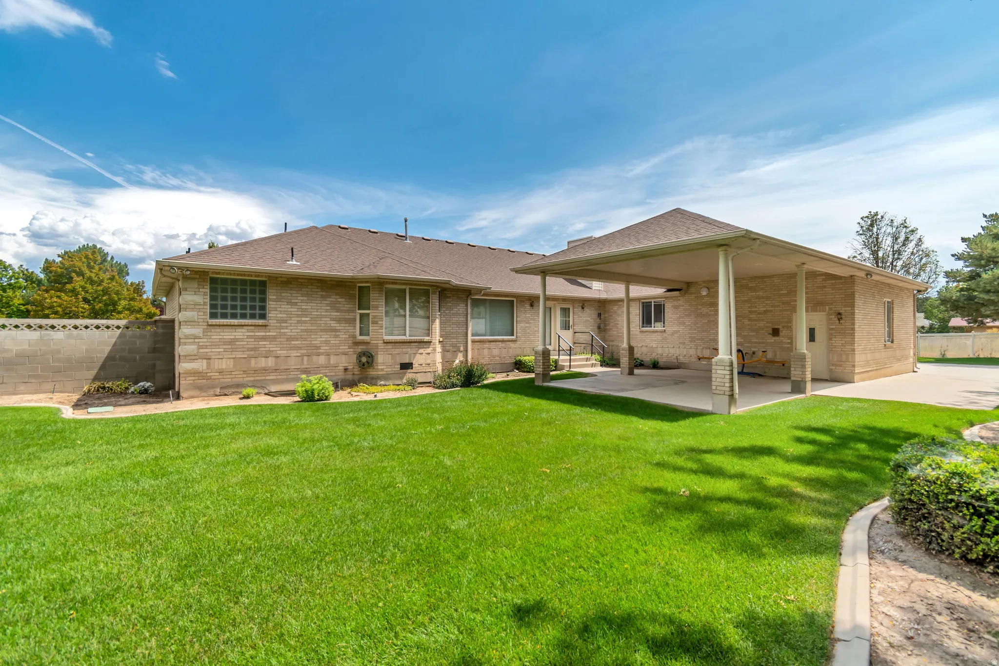 Expansive green lawn with mature landscaping, covered patio, and brick exterior
