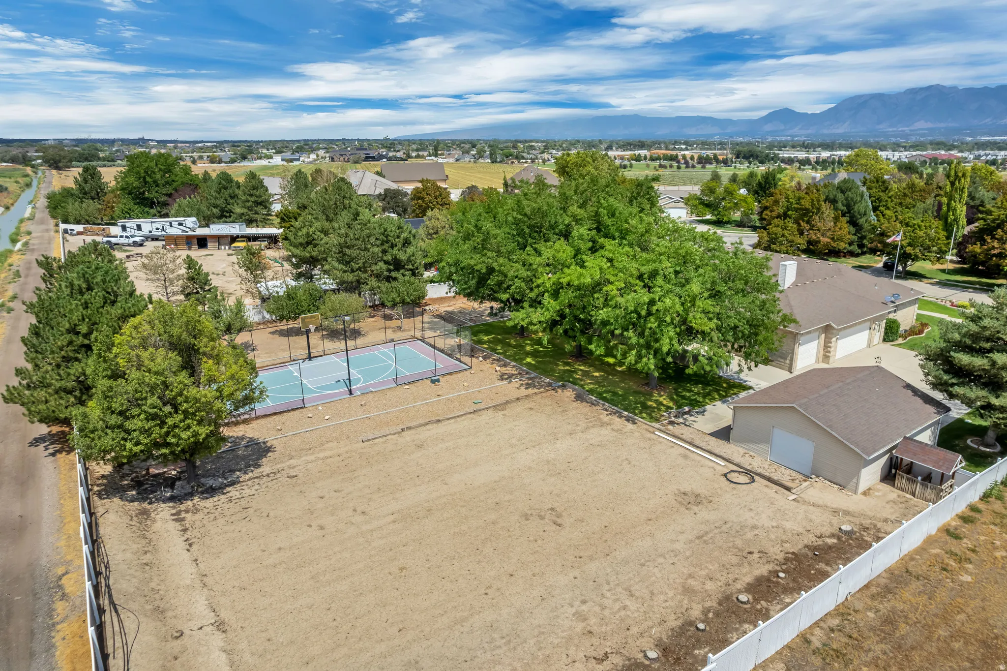 Expansive lot featuring a full-size sports court, mature trees, an attached garage, and a detached outbuilding