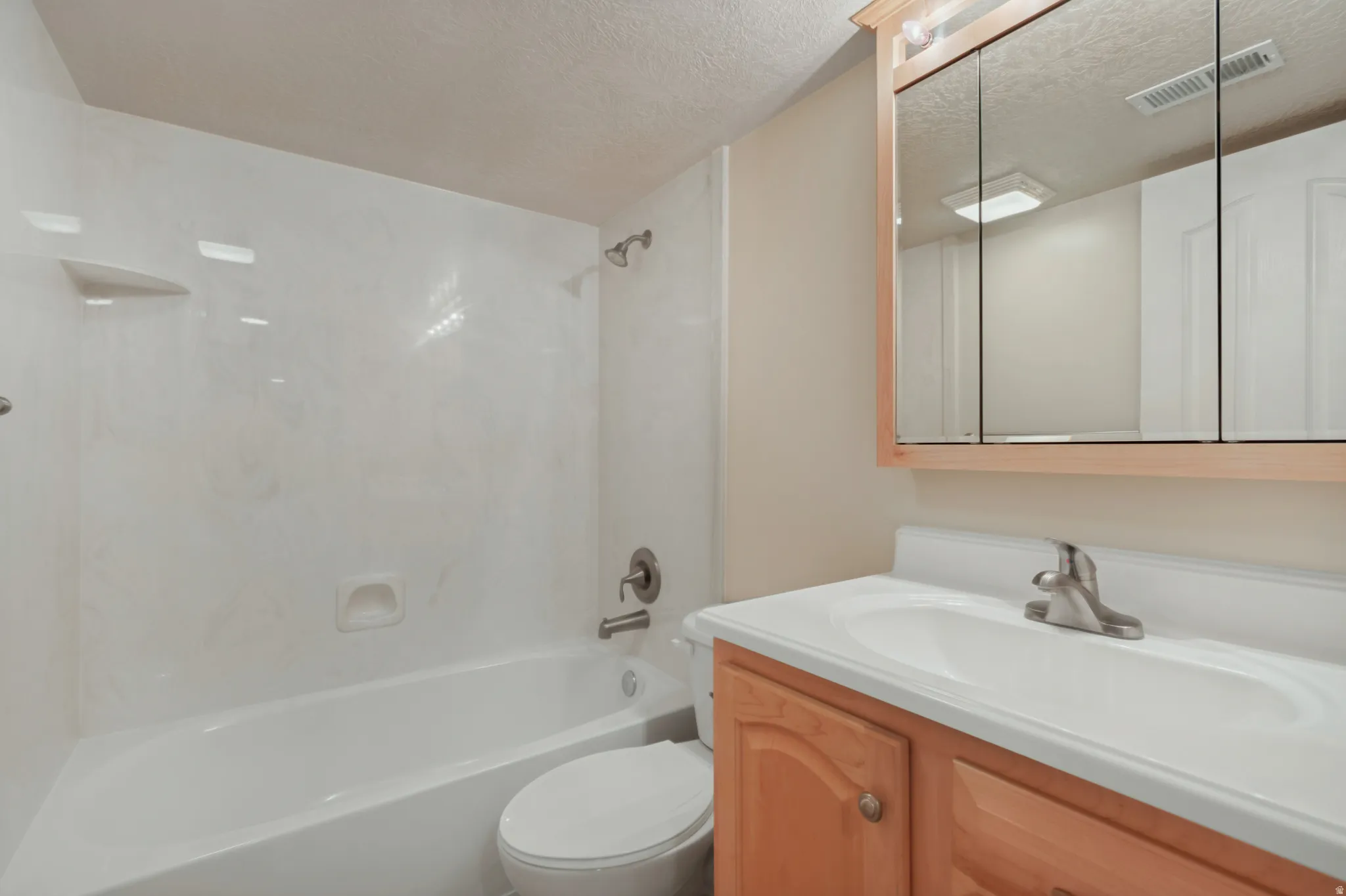 Integrated tub/shower combination, wood-finish vanity with a single sink, and a mirrored medicine cabinet