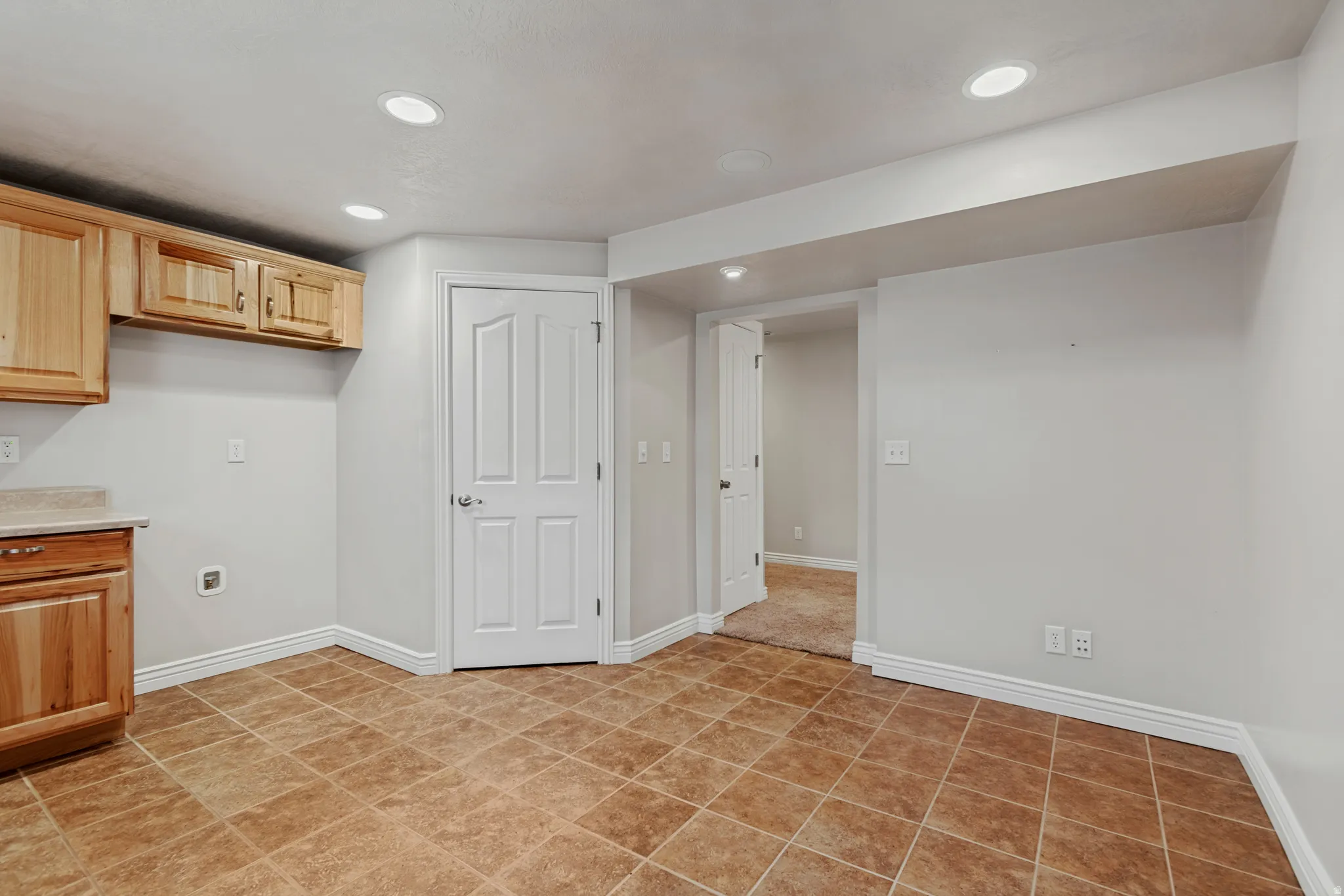 Recessed lighting, wood cabinetry, light-toned countertop, panel doors, and tile flooring