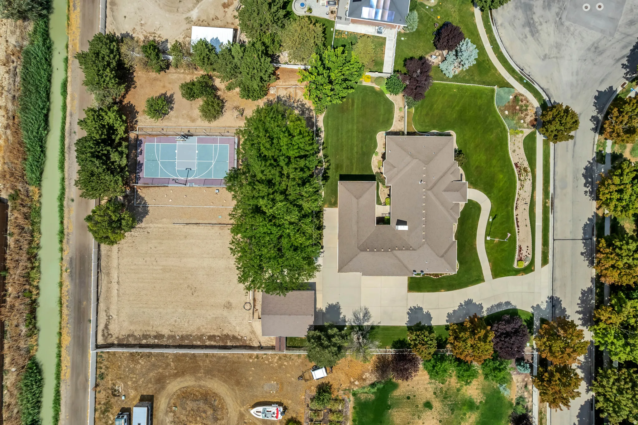 Expansive property featuring a basketball court, mature trees, a detached auxiliary structure, and a large paved driveway