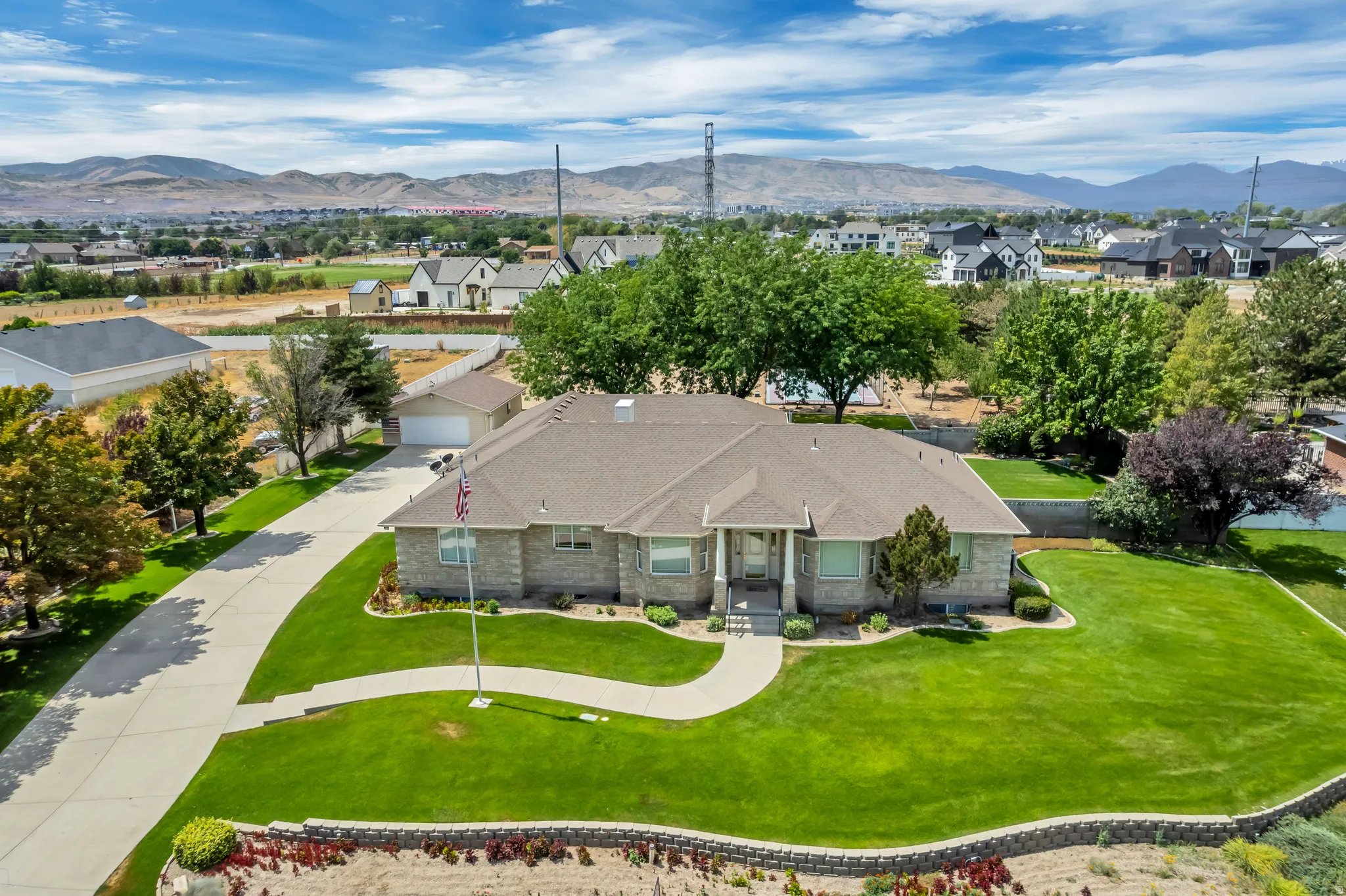 Stone-clad exterior, curved concrete driveway, attached garage, sloped lawn, and mature trees