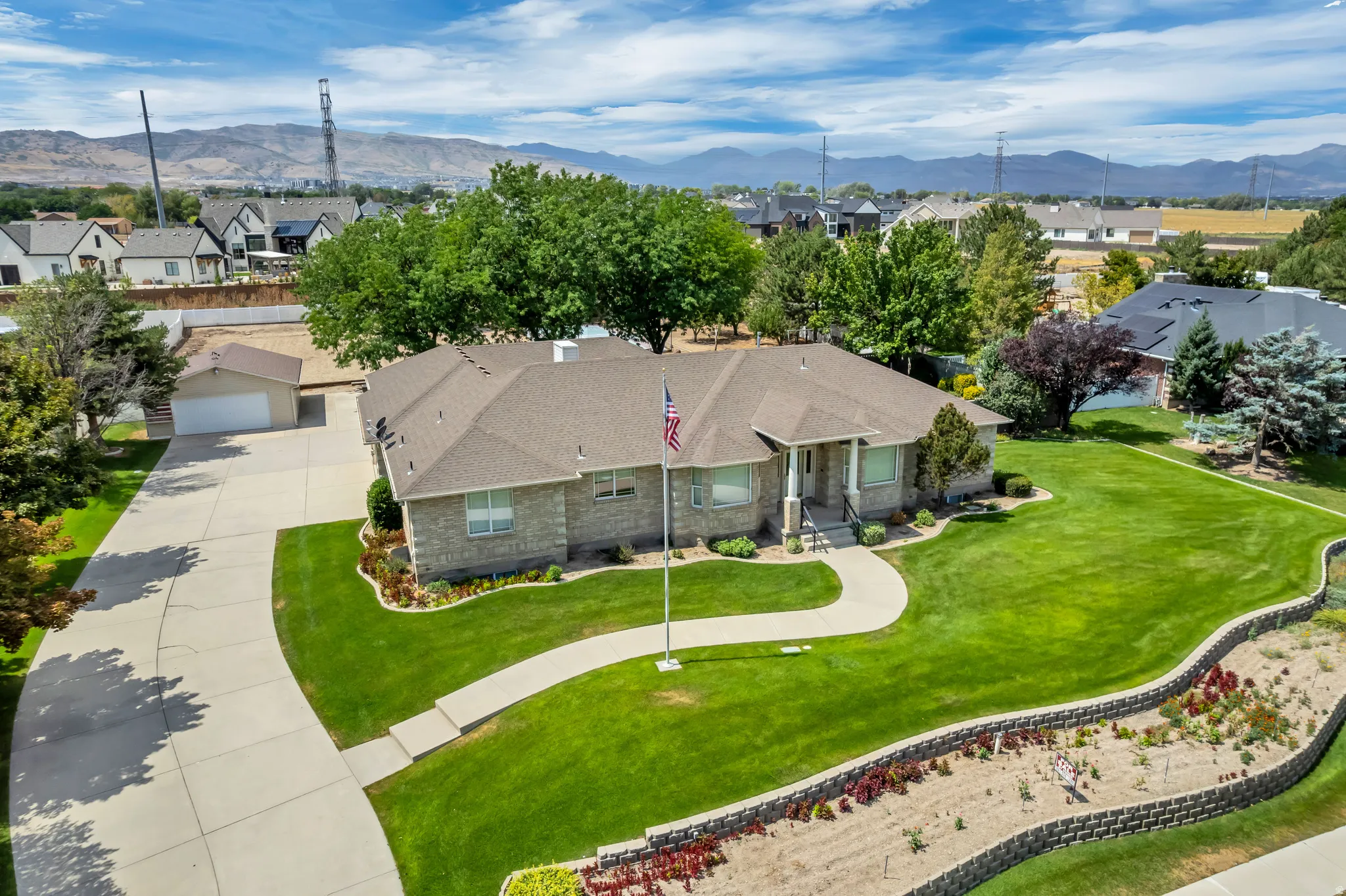 Stone veneer exterior with a hip roof, featuring a curved concrete walkway, expansive lawn, and a retaining wall with landscaping
