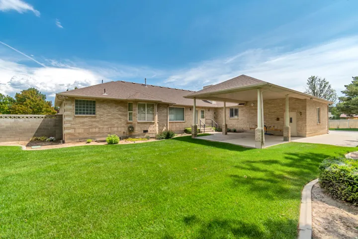 Expansive green lawn with mature landscaping, covered patio, and brick exterior