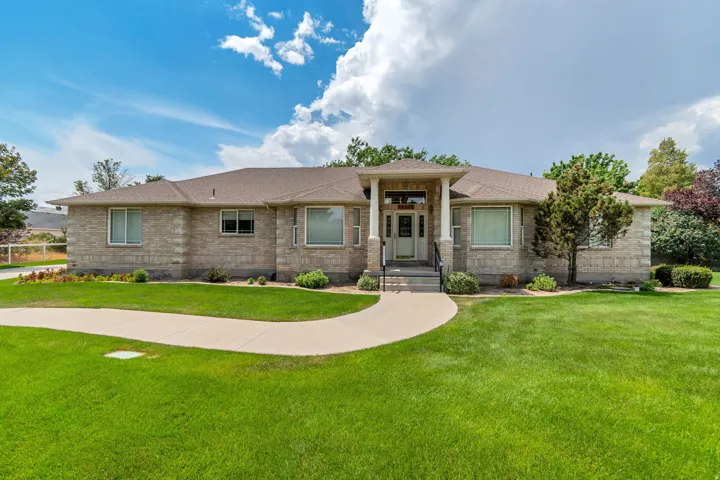 Stone exterior, columned portico, concrete walkway, established landscaping, and a manicured lawn