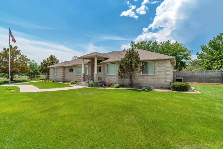 Single-story stone exterior, columned front entry, mature front landscaping, expansive green lawn, and concrete pathway
