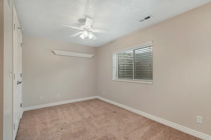 Ceiling fan with integrated lighting, window with blinds, wall shelving, light-toned carpeting, and neutral wall color