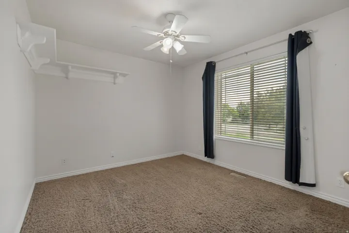 Neutral wall finishes, carpet flooring, window with horizontal blinds, built-in shelving, and a ceiling fan with integrated lighting