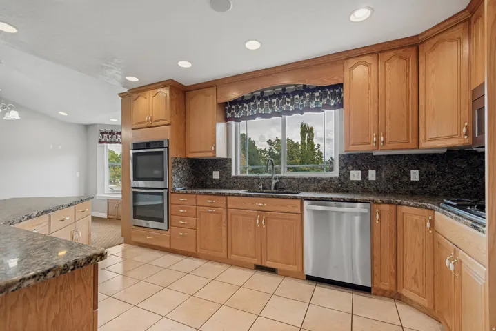 Kitchen featuring natural wood cabinetry, dark speckled countertops, stainless steel double wall ovens, a stainless steel dishwasher, and tile flooring