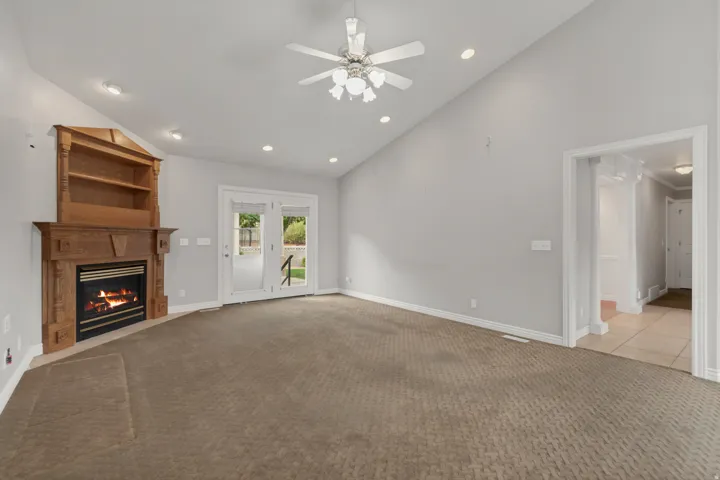 Vaulted ceiling with recessed lighting, corner fireplace with built-in shelving, glass French doors, and ceiling fan