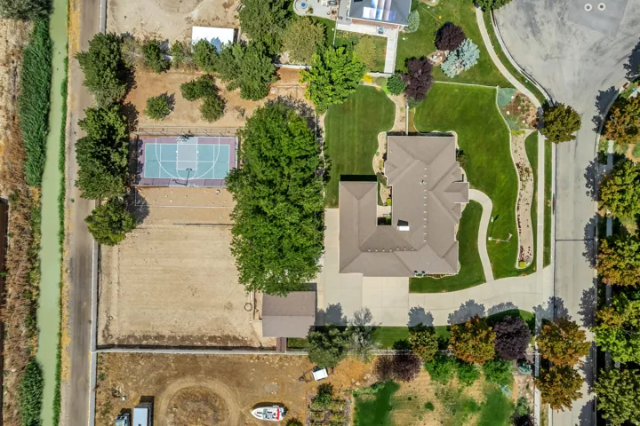 Expansive property featuring a basketball court, mature trees, a detached auxiliary structure, and a large paved driveway