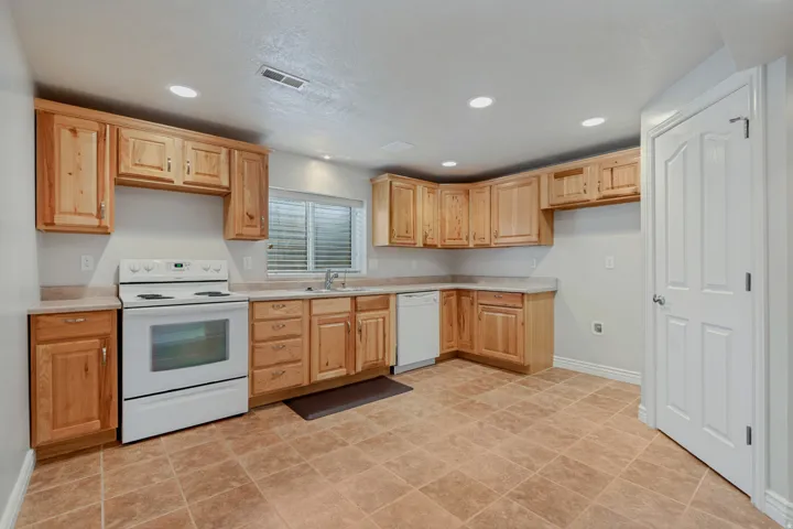 Full kitchen featuring wood cabinetry, solid surface countertops, a white range, white dishwasher, and tiled flooring