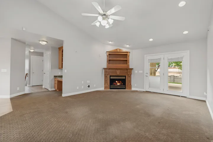 Vaulted ceiling, ceiling fan, recessed lighting, corner fireplace with wood mantel and built-in shelving, and French doors