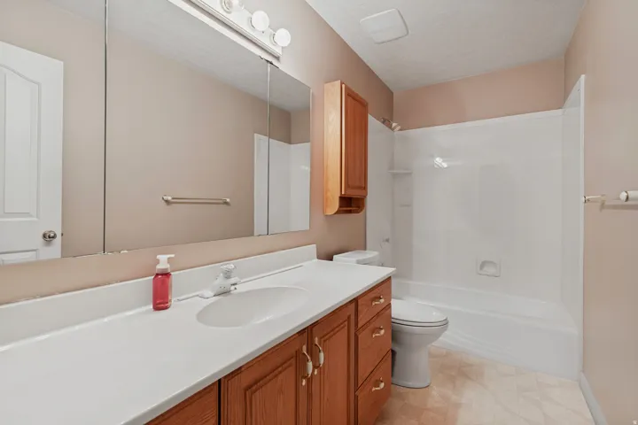 Vanity with an integrated sink and white countertop, wood-finish cabinetry, a large wall-mounted mirror, and a full bathtub with shower