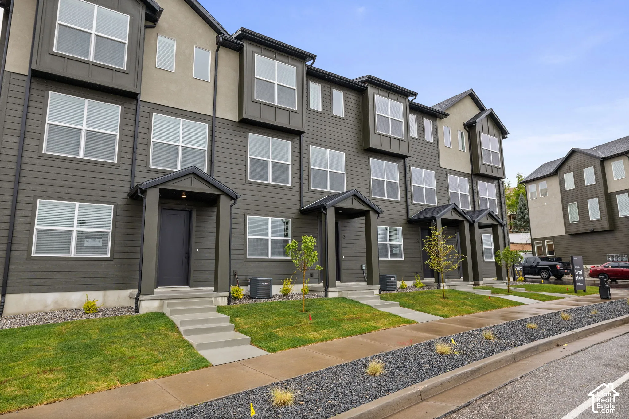 Contemporary townhome exterior featuring multi-toned siding, projecting bay windows, a covered entry, and a concrete walkway