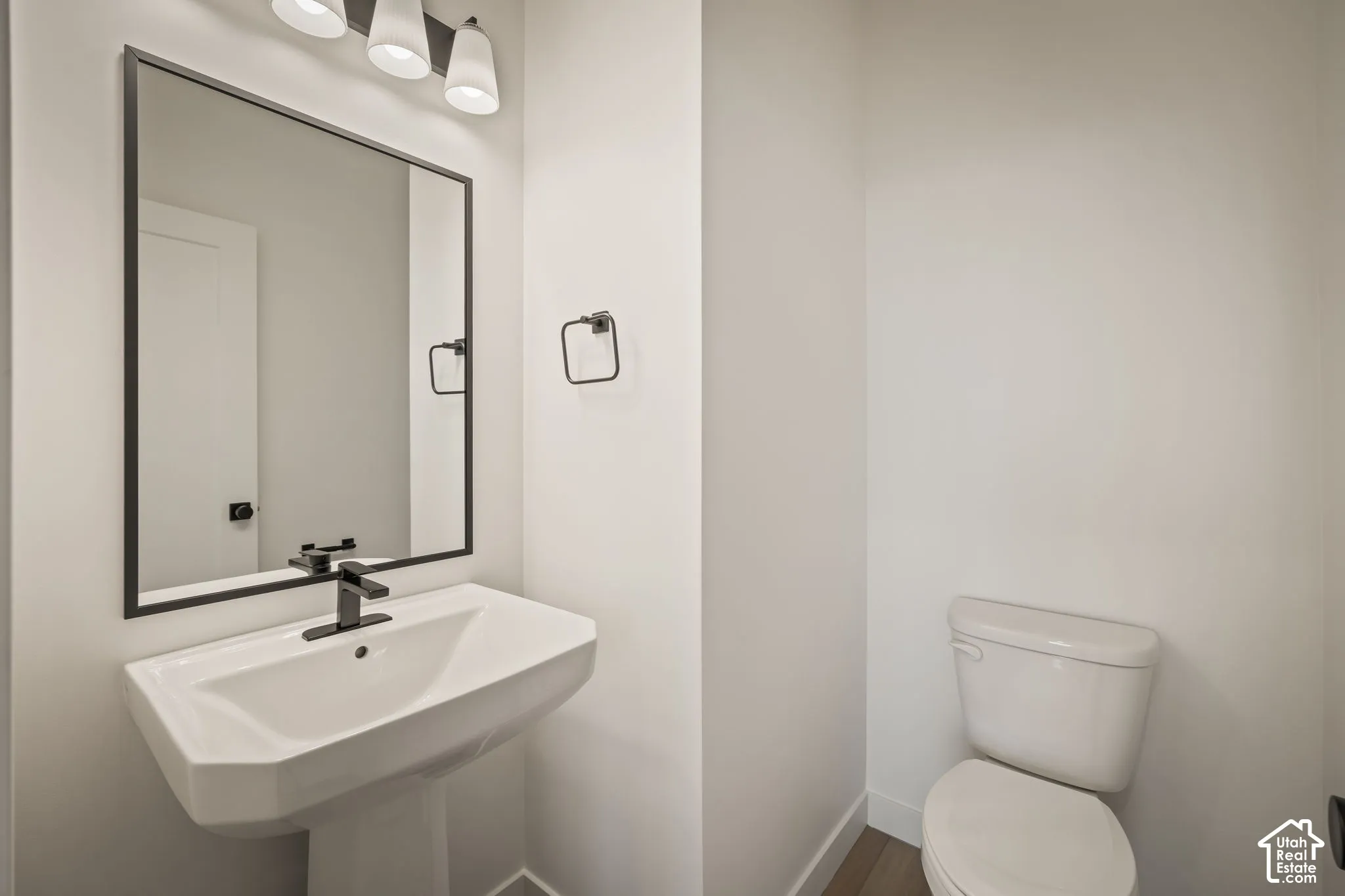 Pedestal sink with a matte black faucet, framed mirror, and a three-light vanity fixture