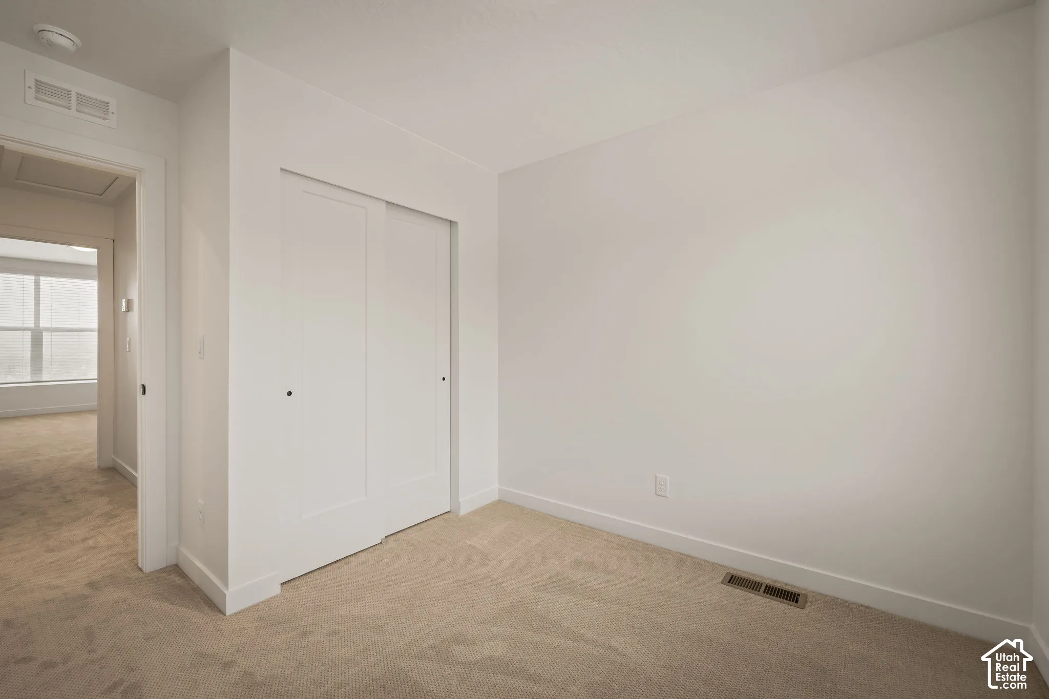 Neutral wall color with plush carpeting, featuring a built-in closet with sliding doors and white trim