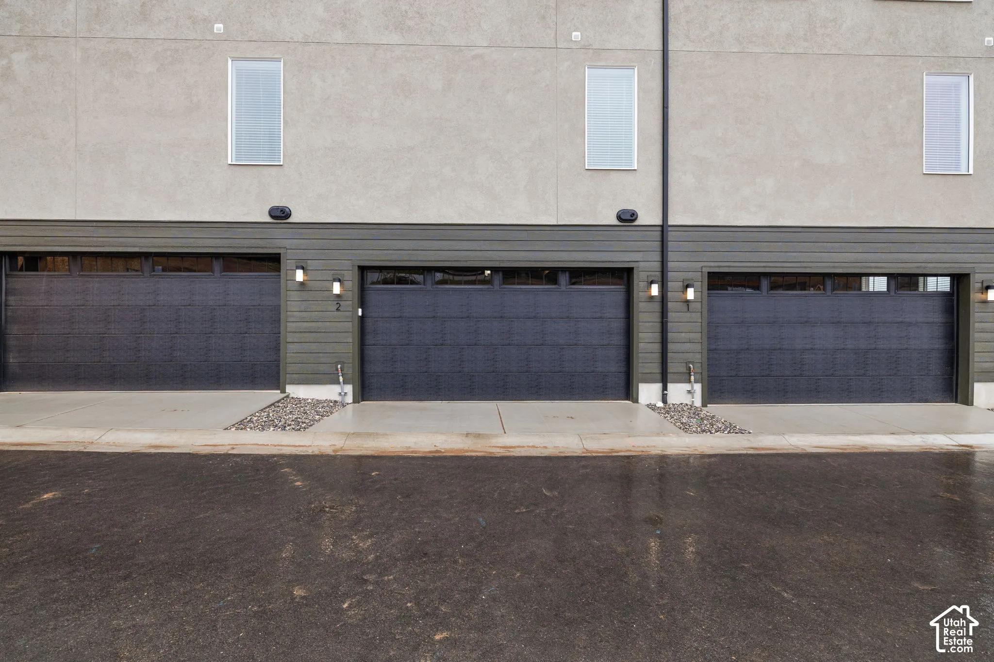 Multiple garage doors with transom windows, concrete driveways, and modern wall-mounted lighting fixtures