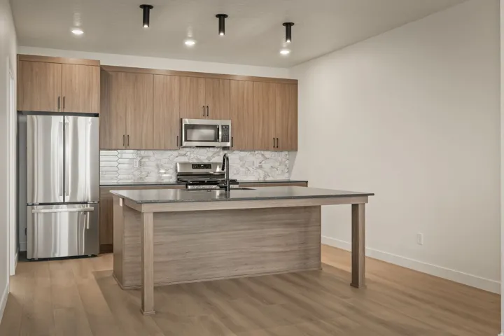 Modern kitchen with wood-finish cabinetry, stainless steel appliances, and a central island with a sink