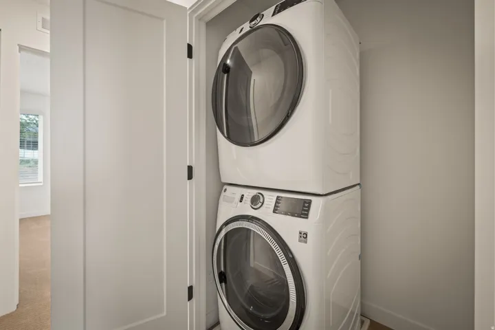 Stacked washer and dryer within a dedicated closet space, featuring white flat-panel doors and matte black hardware
