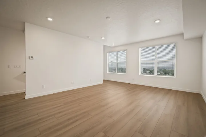 Recessed lighting, wood-finish flooring, two windows with blinds, and white wall finishes