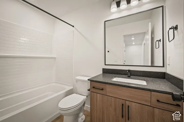 Bathtub with white subway tile surround, wood-finish vanity with dark countertop, integrated rectangular sink, matte black faucet, and rectangular mirror with black frame