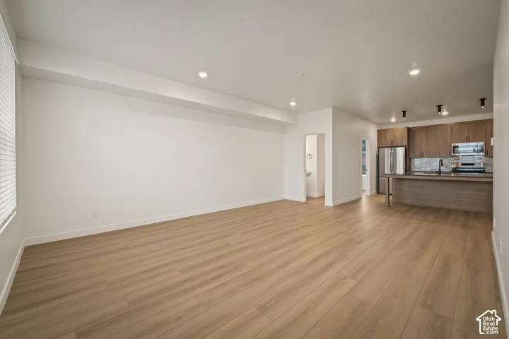 Recessed lighting, wood-finish flooring, white walls, wood-finish cabinetry, and stainless steel appliances