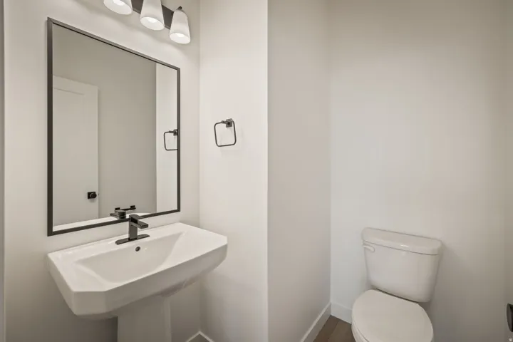 Pedestal sink with a matte black faucet, framed mirror, and a three-light vanity fixture