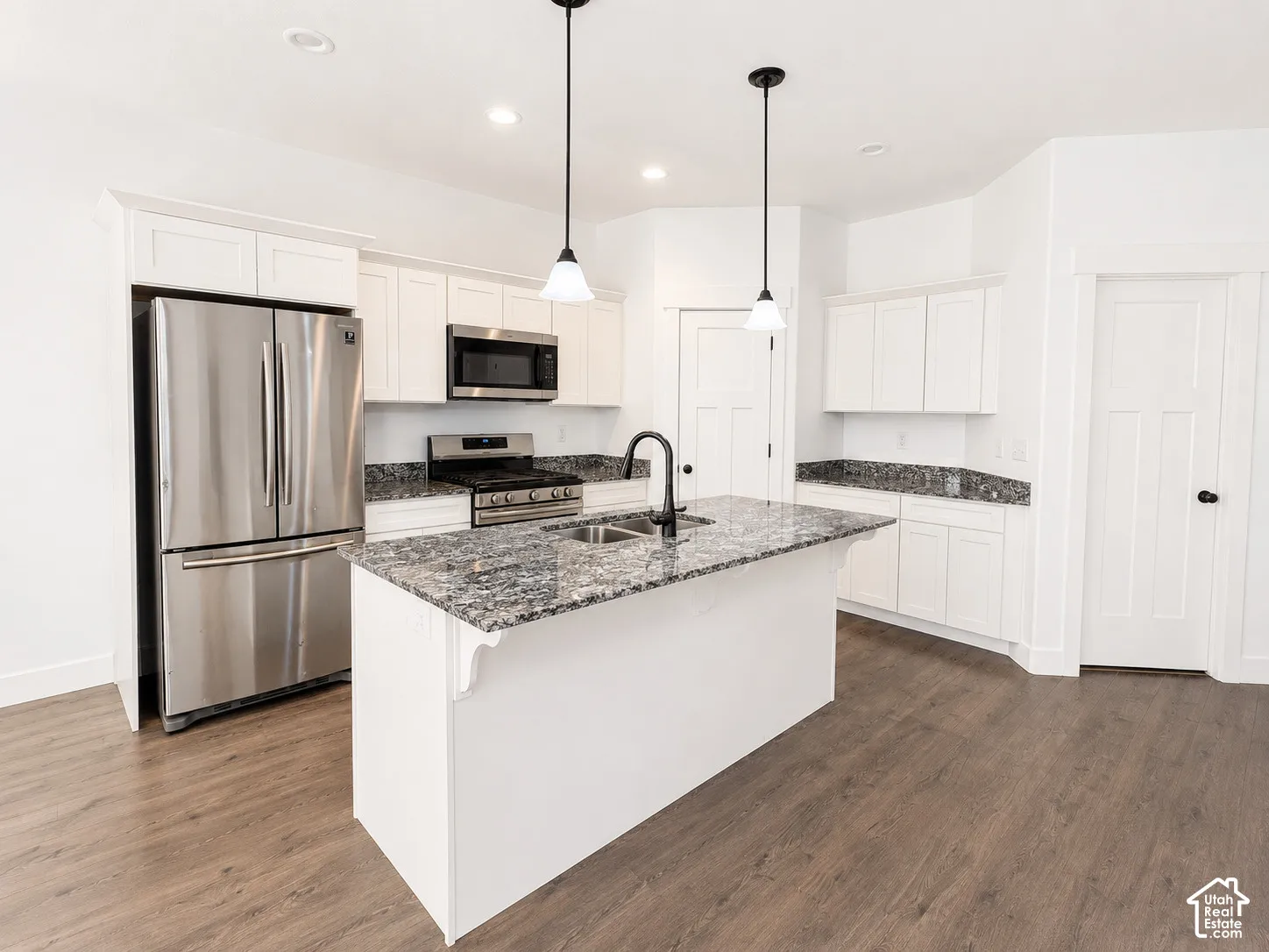 Kitchen featuring an island, stainless steel appliances, white cabinetry, wood-finish flooring, and pendant lighting