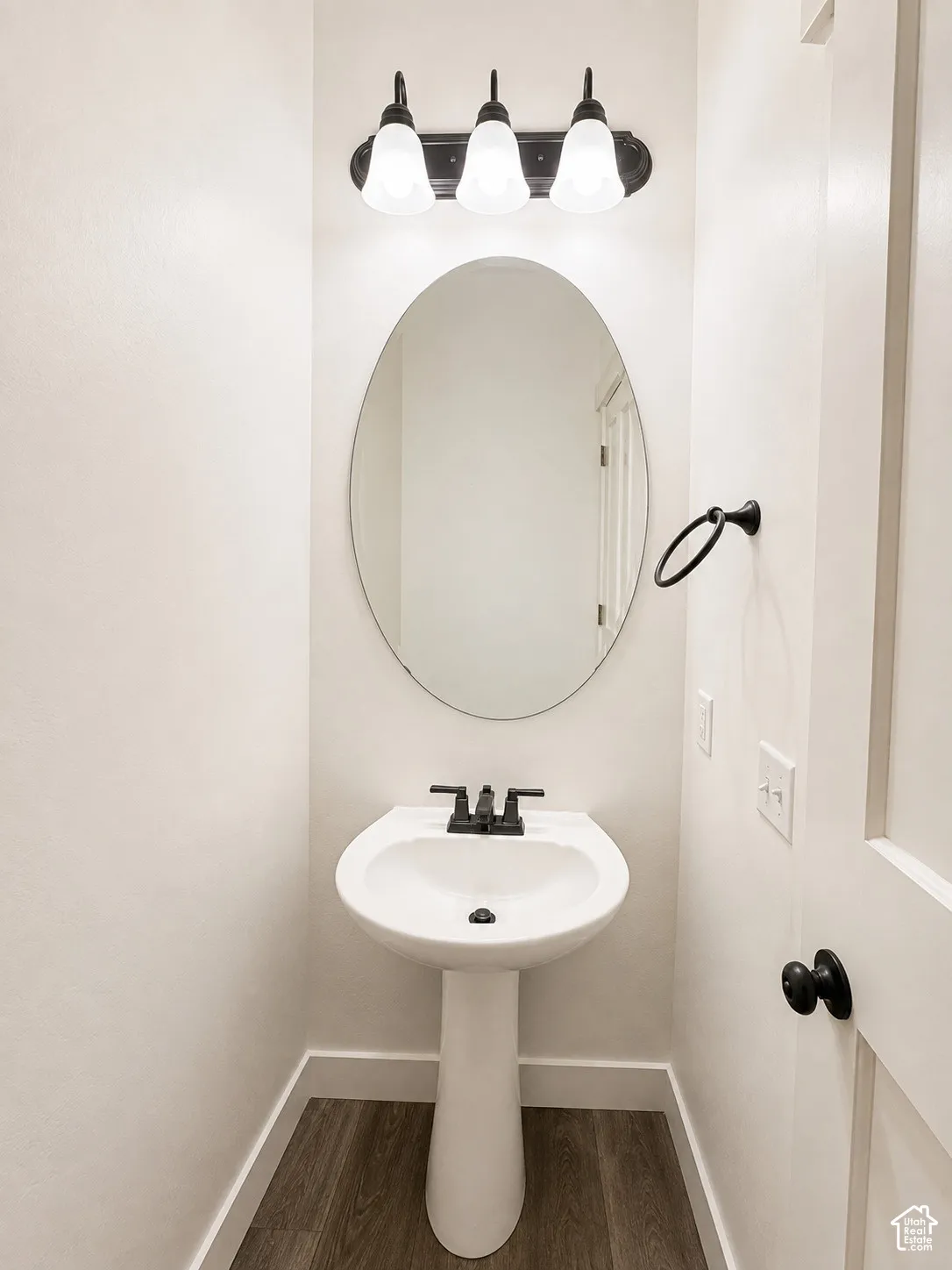 White pedestal sink with a matte black faucet, oval mirror, and a three-light vanity fixture