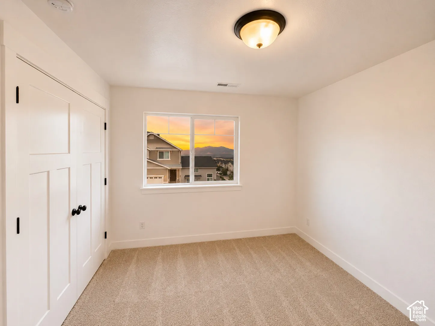 Neutral wall tones, carpeted flooring, window with white trim, white paneled bifold closet doors, and a ceiling-mounted light fixture