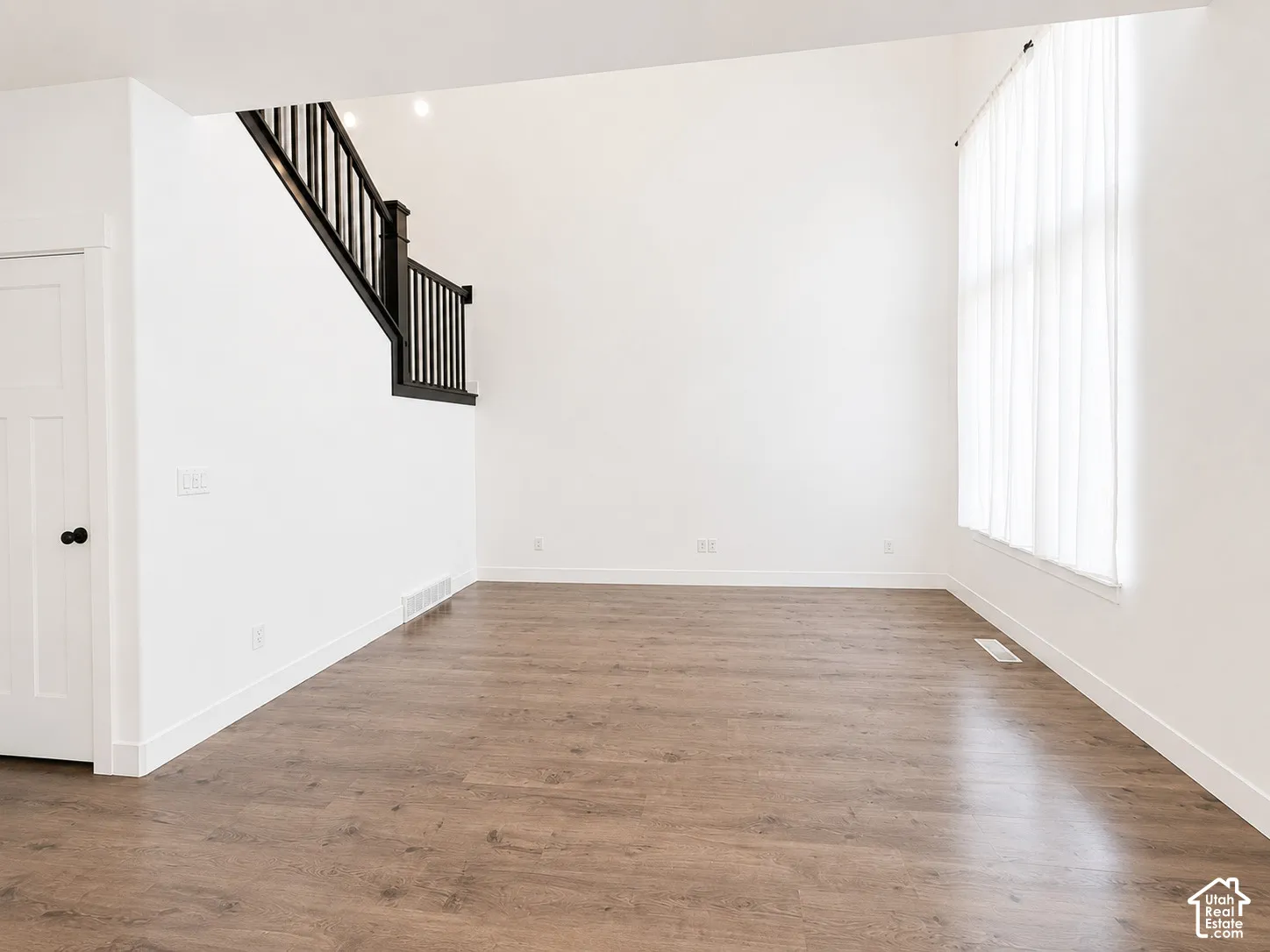Spacious room featuring vaulted ceilings, wood-finish flooring, a two-panel interior door, and a staircase with dark wood newel posts and balusters