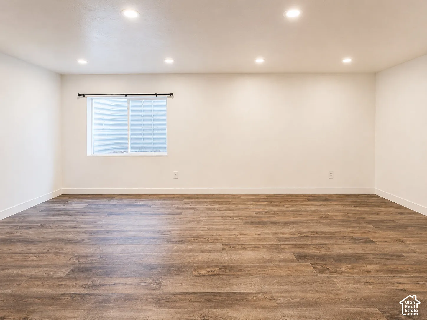 Recessed ceiling lighting, wood-finish flooring, white walls, and a window with a window well