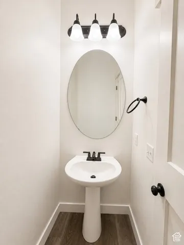 White pedestal sink with a matte black faucet, oval mirror, and a three-light vanity fixture