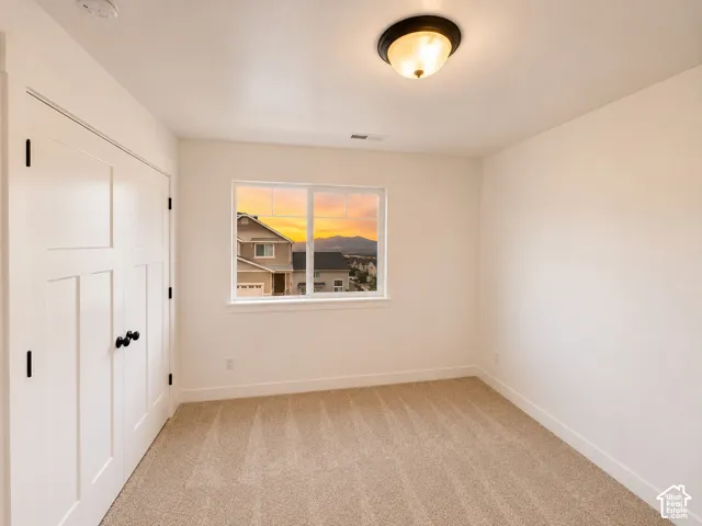 Neutral wall tones, carpeted flooring, window with white trim, white paneled bifold closet doors, and a ceiling-mounted light fixture