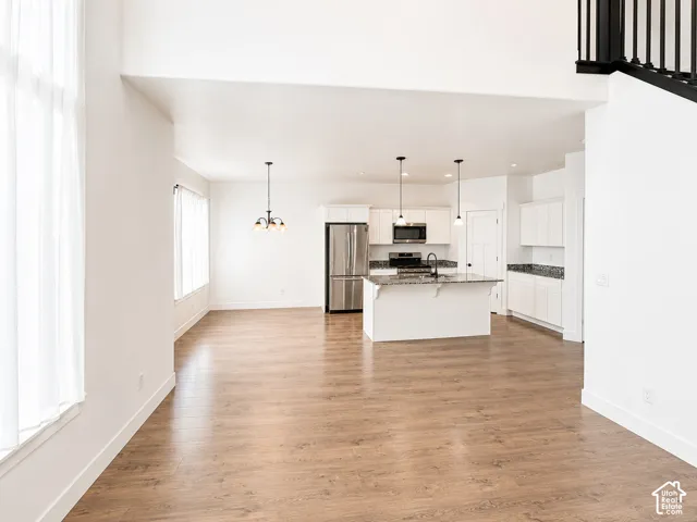High ceilings, wood-finish flooring, white cabinetry, stainless steel appliances, and a kitchen island with stone countertops