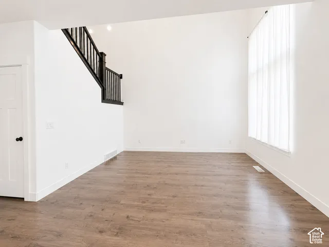 Spacious room featuring vaulted ceilings, wood-finish flooring, a two-panel interior door, and a staircase with dark wood newel posts and balusters