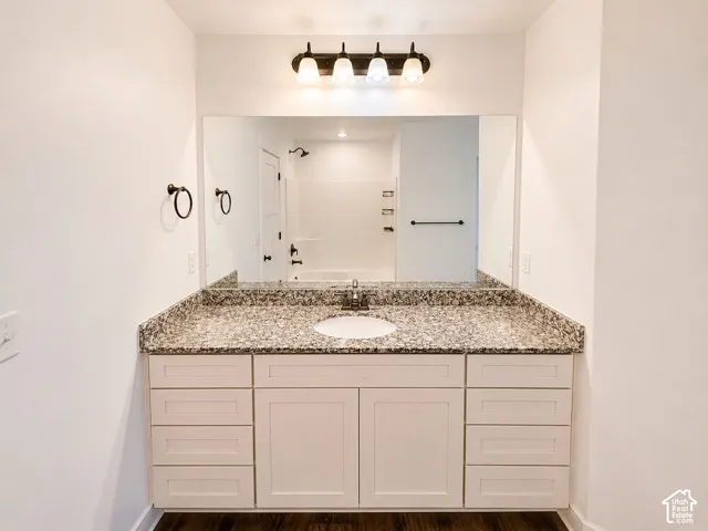 White vanity with integrated sink, granite countertop, wall-mounted mirror, and dark wood-finish flooring