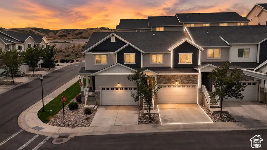 Multi-level townhome featuring a two-car garage, stone facade accents, and a covered entryway