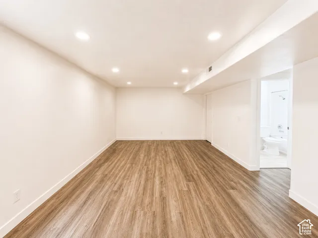 Recessed lighting illuminates the expansive room featuring wood-finish flooring and white walls
