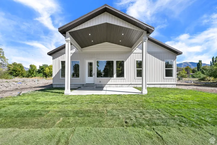 Rear exterior featuring white vertical siding, a covered patio with recessed lighting, multiple large windows, and a glass-paneled door