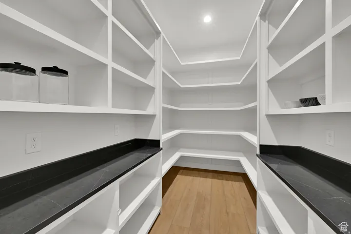 Walk-in pantry featuring extensive built-in shelving, dark countertops, recessed lighting, and wood-finish flooring