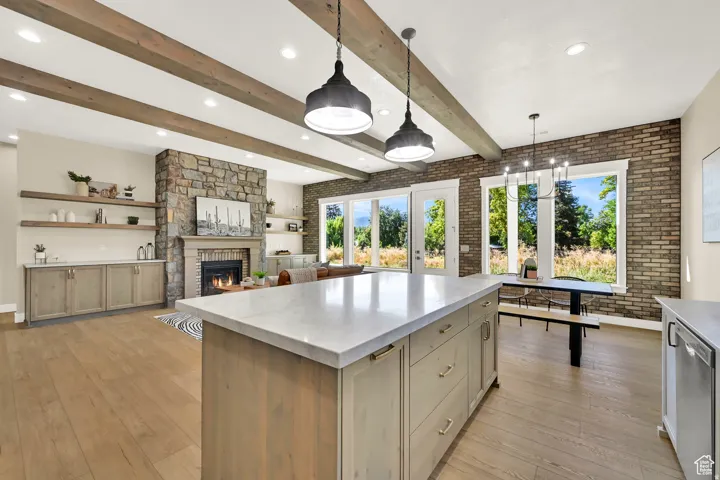 Wood-finish flooring, exposed ceiling beams, stone-clad fireplace, kitchen island with a light-toned countertop, and brick accent wall