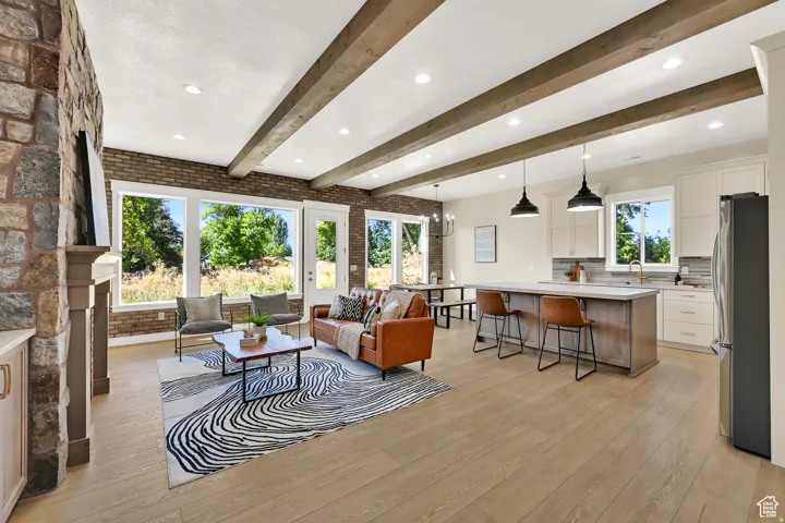 Open-concept living space featuring wood-finish flooring, exposed ceiling beams, and stone accent walls