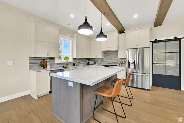 Kitchen featuring white shaker cabinetry, stainless steel appliances, a center island with countertop seating, and wood-finish flooring