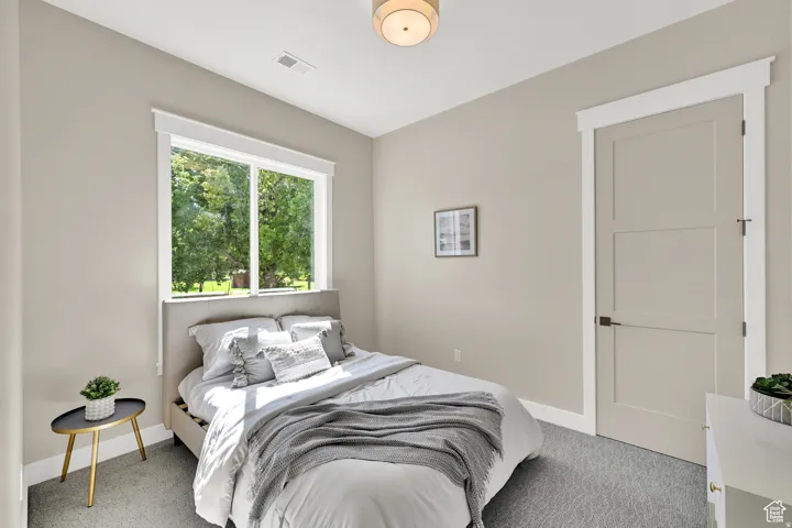 Spacious room featuring a large window, light-colored walls, patterned carpeting, a three-panel interior door, and a flush-mount ceiling light fixture